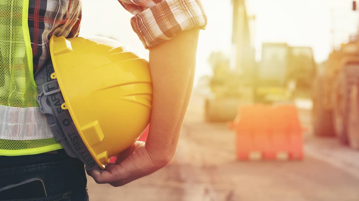 rs=w_800,cg_true,m Worker holding hard hat at sundown, looking at construction site.